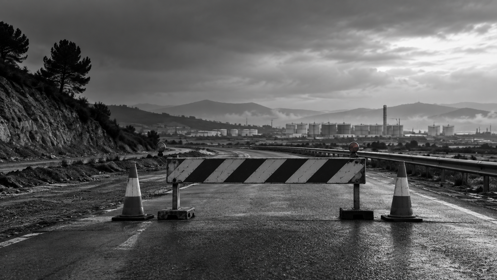 Carretera real cortada por una valla de obras y conos, en blanco y negro